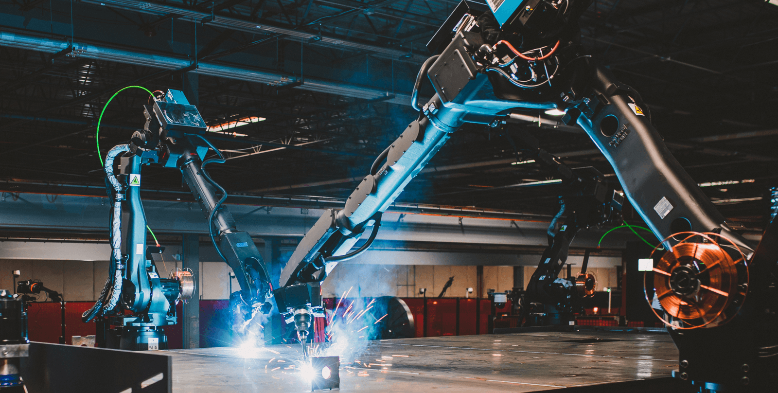 Two industrial robotic arms perform precision welding with bright sparks in a manufacturing facility.